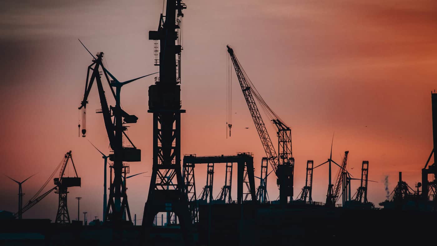 Quay cranes silhouetted against a burning dusk sky over a working port