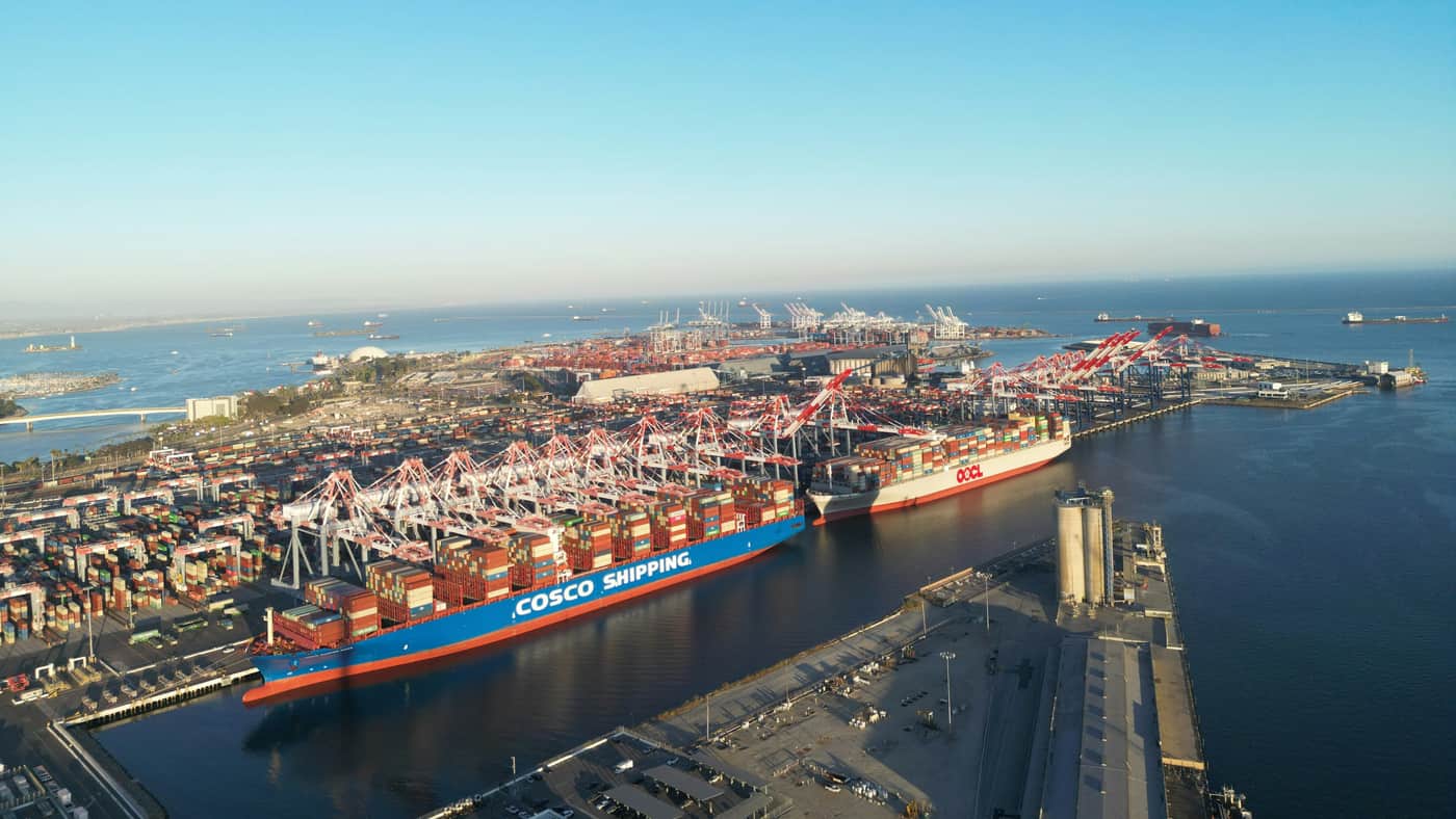 Aerial view of a container terminal at golden hour, ranks of ship-to-shore gantry cranes working a vessel at the berth