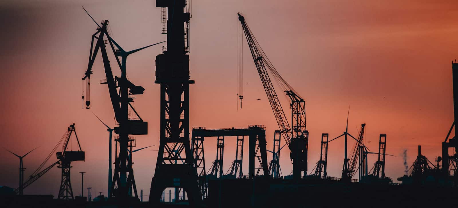 Quay cranes silhouetted against a burning dusk sky over a working port