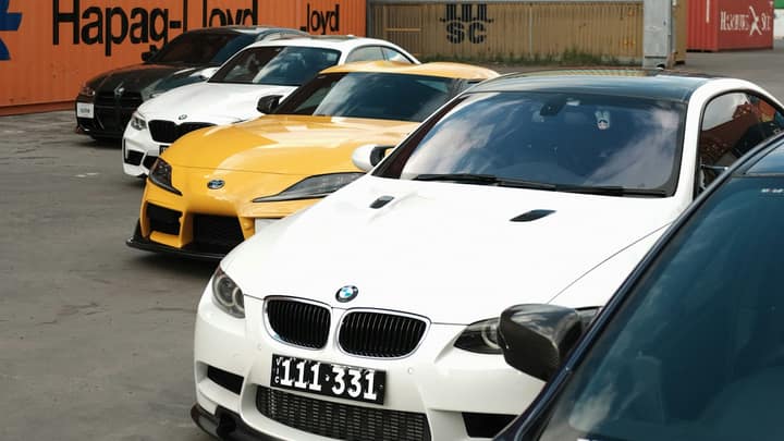 Cars staged for export in front of a wall of shipping containers